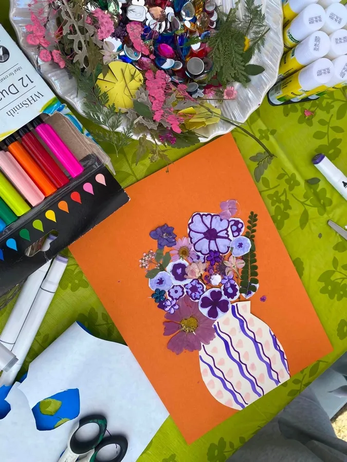 A pressed-flower collage on orange card, surrounded by felt pens and fresh blooms
