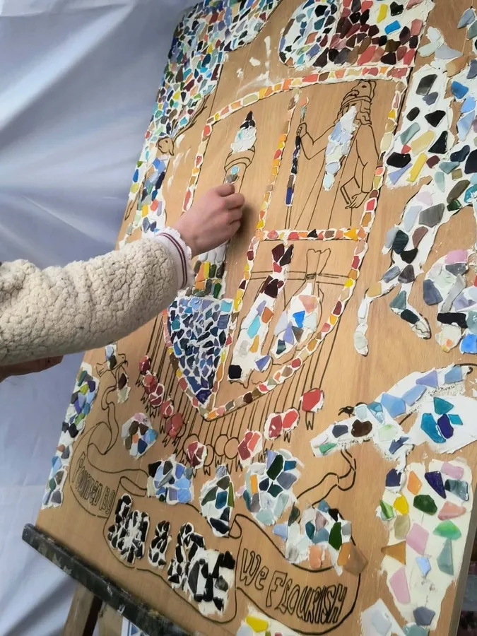 A child's hand pressing mosaic pieces onto a painted wooden panel