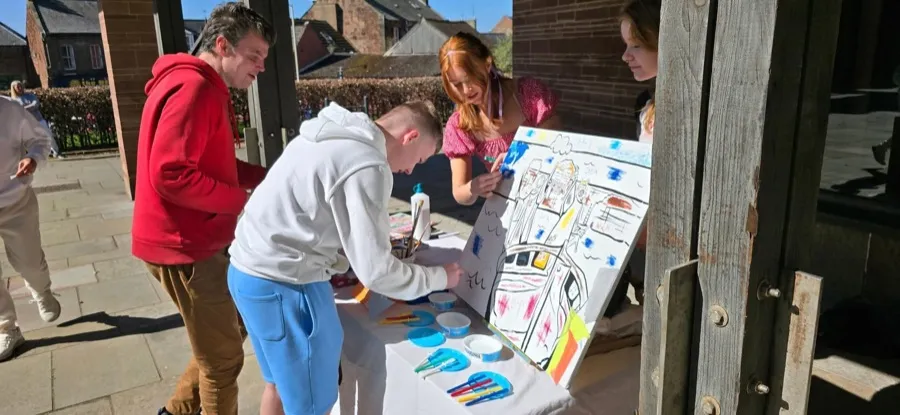 Two children painting and drawing at a workshop table outdoors