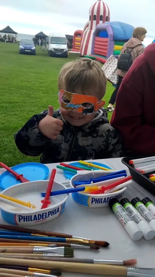 A young maker in face paint giving a thumbs up beside the pens and paints